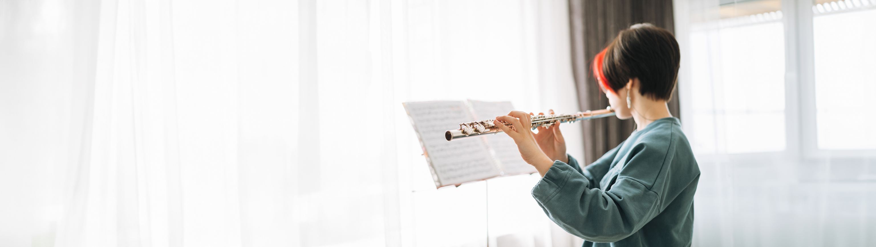 A girl with short red and brown hair playing the flute and reading music on a music stand