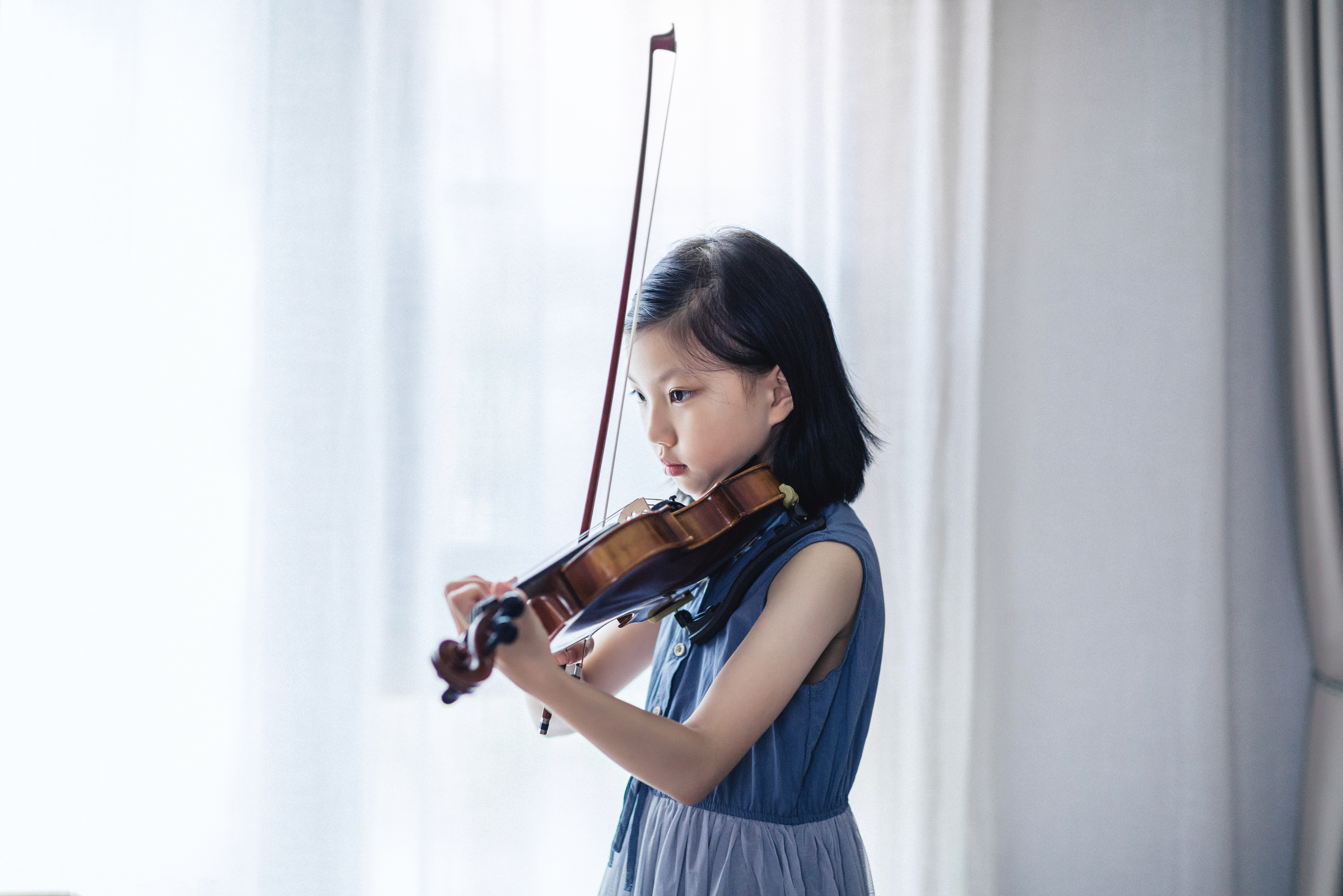 A young girl playing violin in front of a window