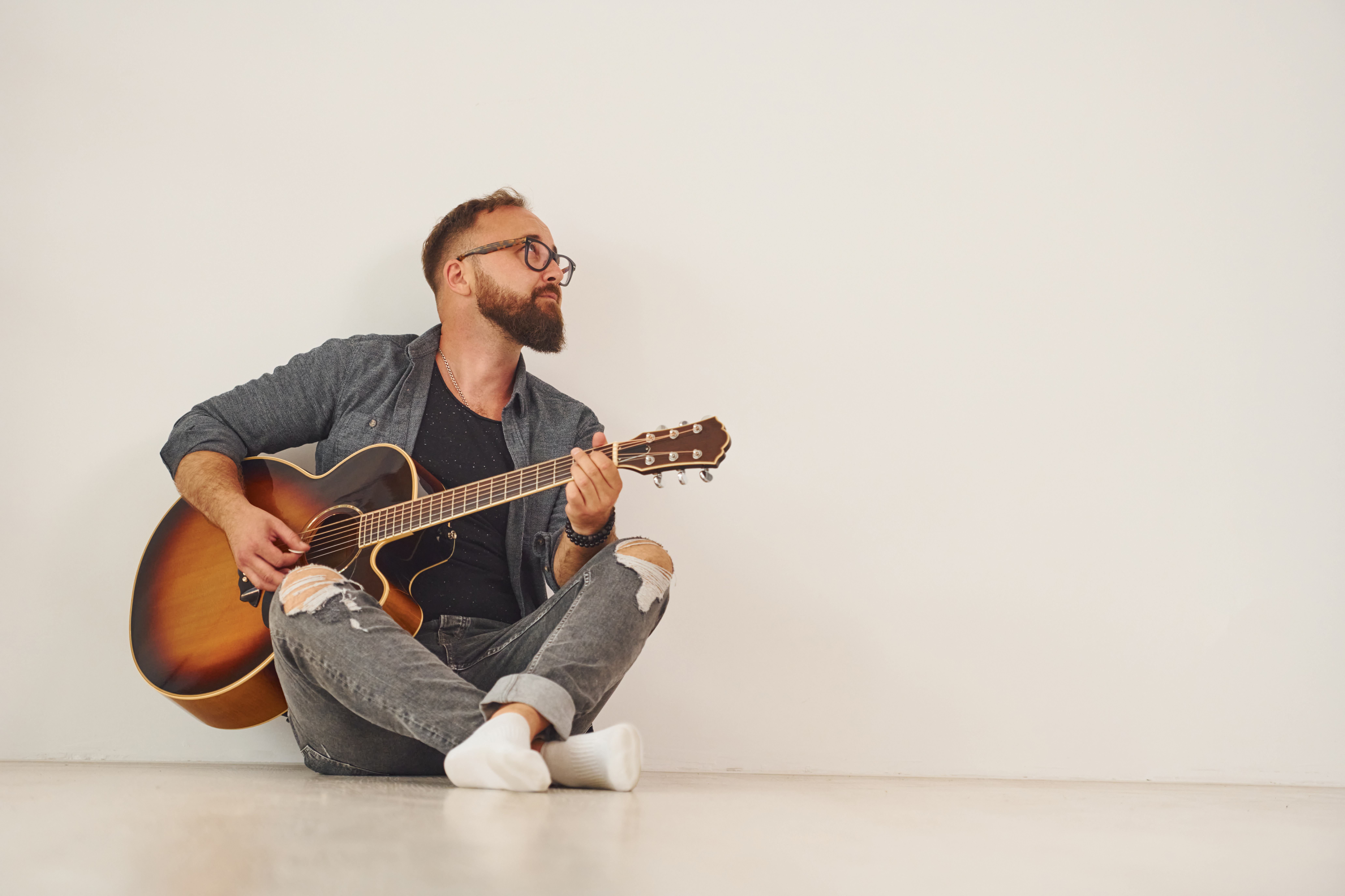 Man sitting on the floor, playing the guitar, in front of a white background