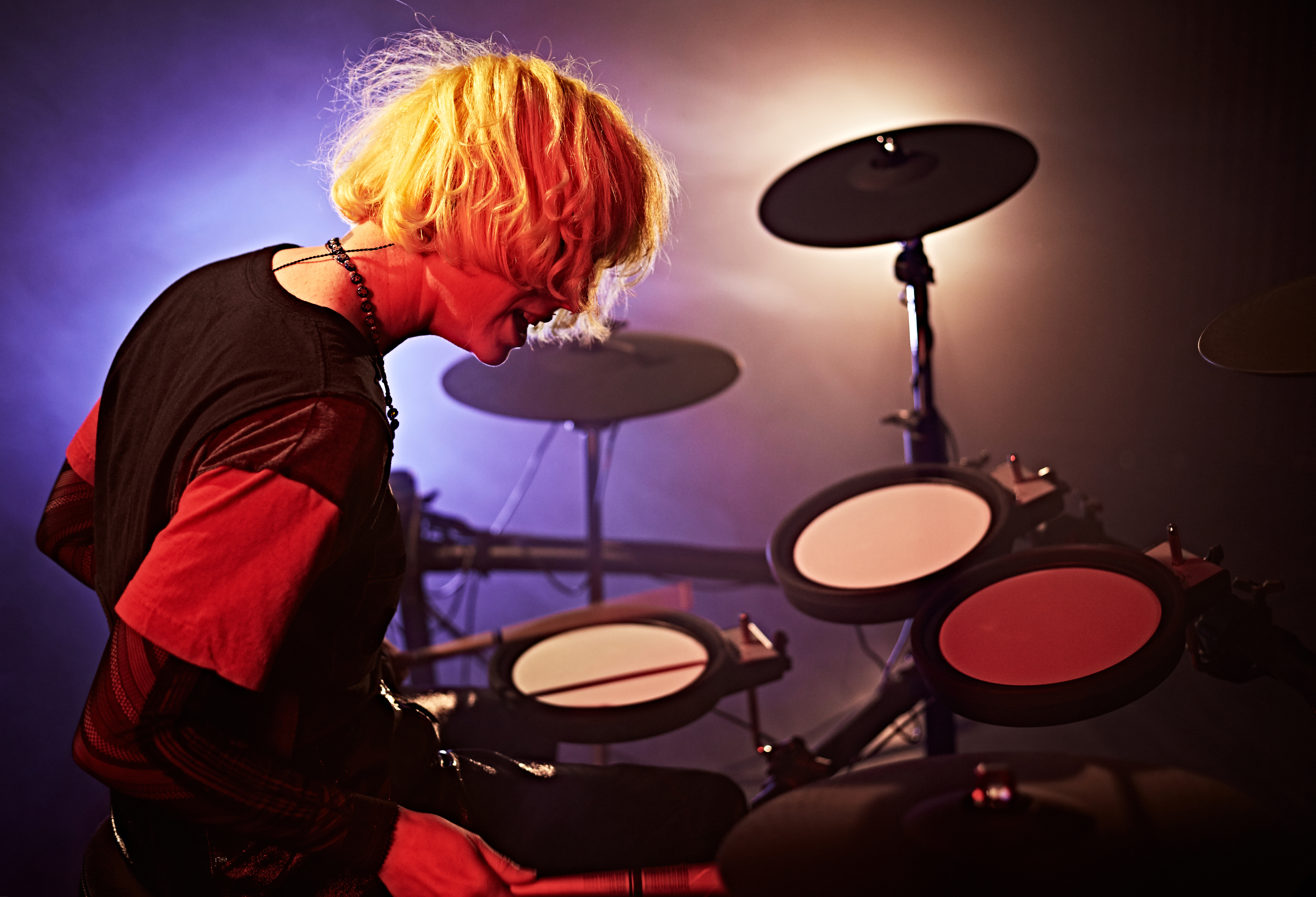 Man with long blonde hair playing an electric drum kit