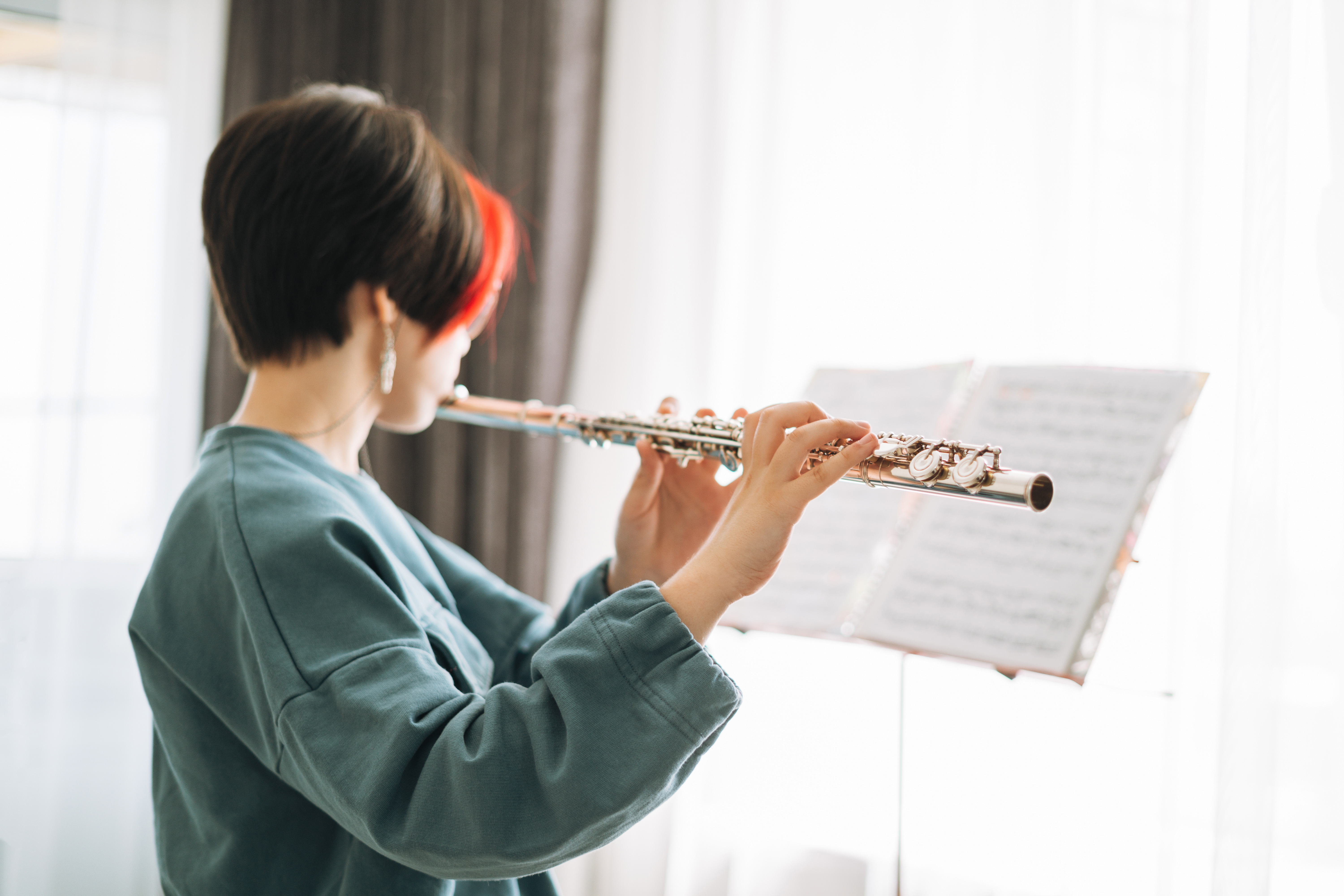 A girl with short red and brown hair playing the flute and reading music on a music stand
