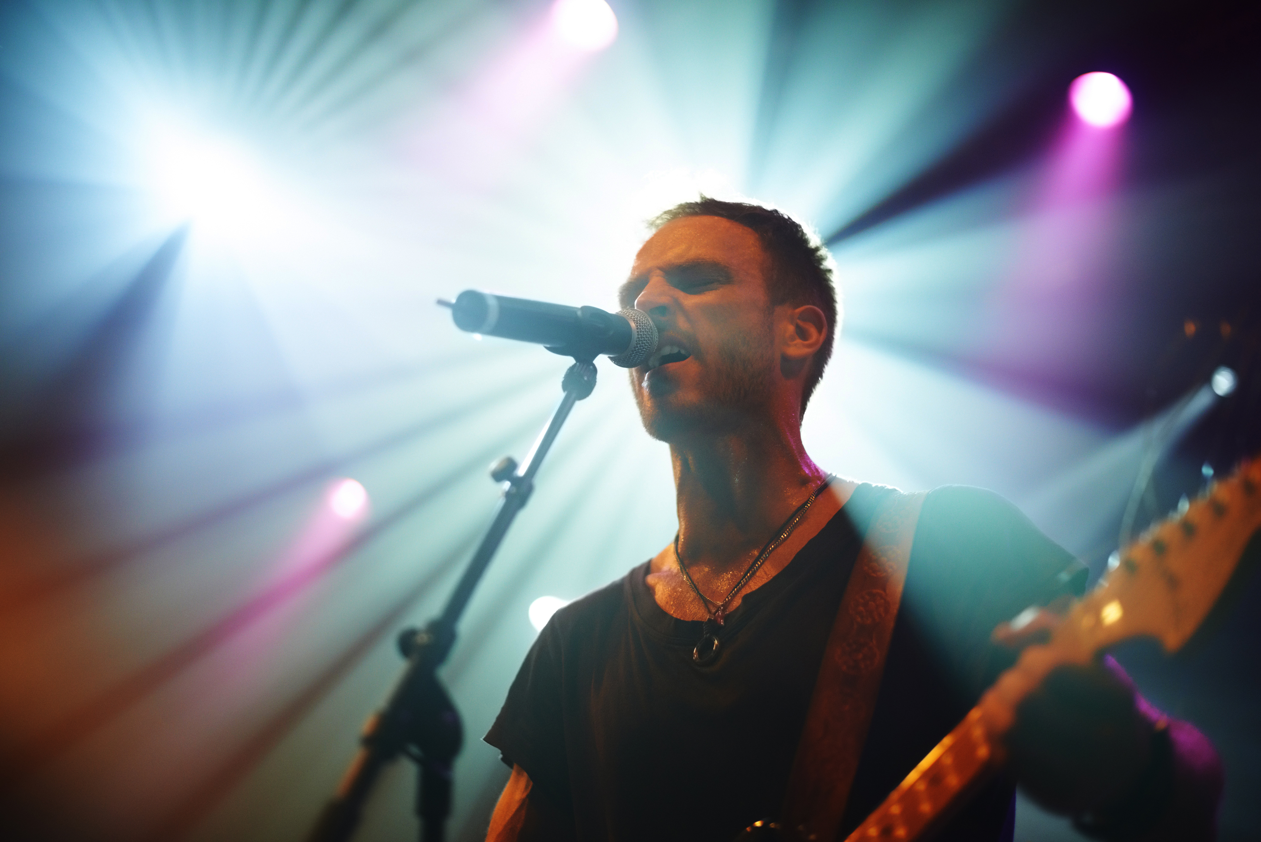 A man on stage performing live, singing into a microphone and playing guitar